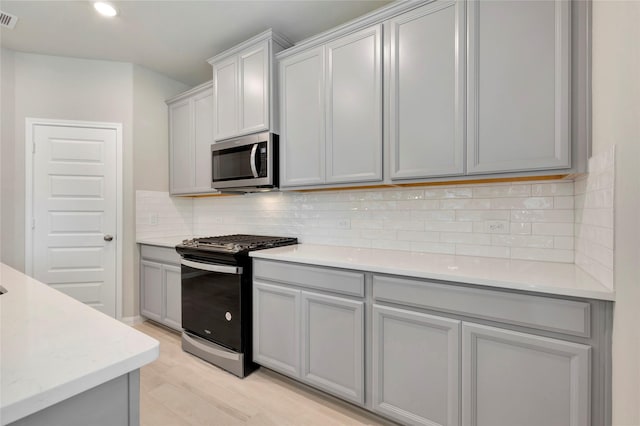 kitchen with decorative backsplash, appliances with stainless steel finishes, light wood-type flooring, and gray cabinetry