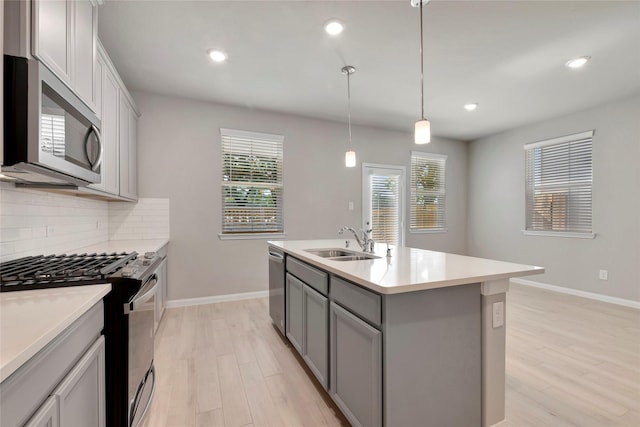 kitchen with sink, backsplash, stainless steel appliances, an island with sink, and decorative light fixtures