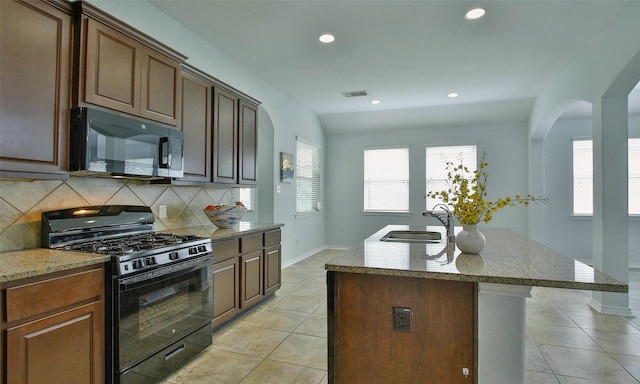 kitchen with backsplash, sink, black appliances, light tile patterned floors, and an island with sink