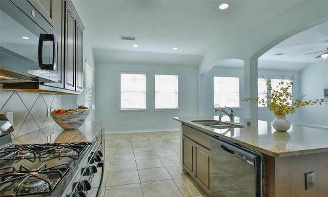 kitchen with gas range, light stone countertops, dishwasher, sink, and an island with sink