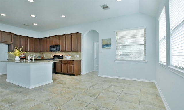 kitchen featuring gas range, light stone countertops, decorative backsplash, a center island with sink, and light tile patterned flooring