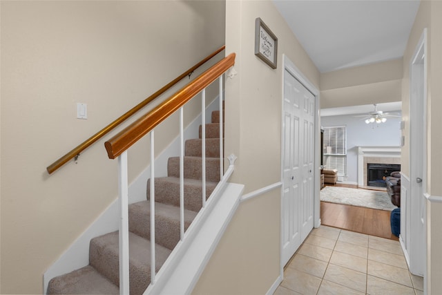 stairway featuring tile patterned flooring, ceiling fan, and a tiled fireplace