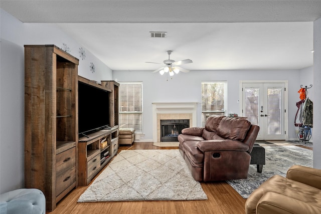 living room featuring a tile fireplace, french doors, light wood-type flooring, and ceiling fan