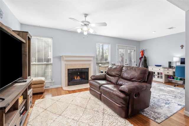 living room featuring a fireplace, ceiling fan, french doors, and light wood-type flooring