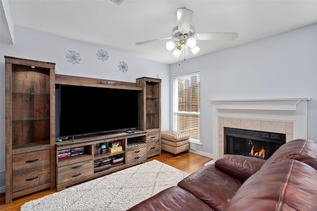 living room with a tile fireplace, light wood-type flooring, and ceiling fan