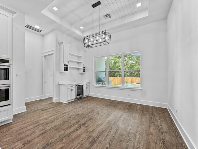 kitchen with white cabinets, double wall oven, a tray ceiling, decorative light fixtures, and beverage cooler