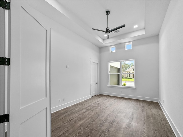 spare room featuring a tray ceiling, ceiling fan, and dark wood-type flooring