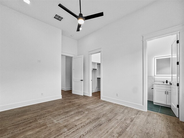 unfurnished bedroom with hardwood / wood-style floors, ceiling fan, a walk in closet, and connected bathroom