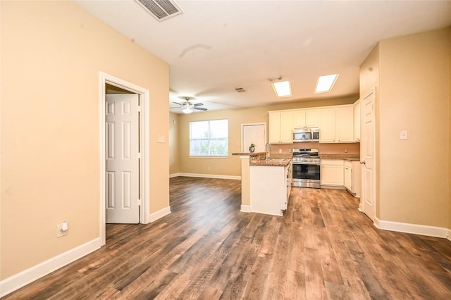 kitchen with appliances with stainless steel finishes, dark hardwood / wood-style flooring, ceiling fan, white cabinets, and a center island