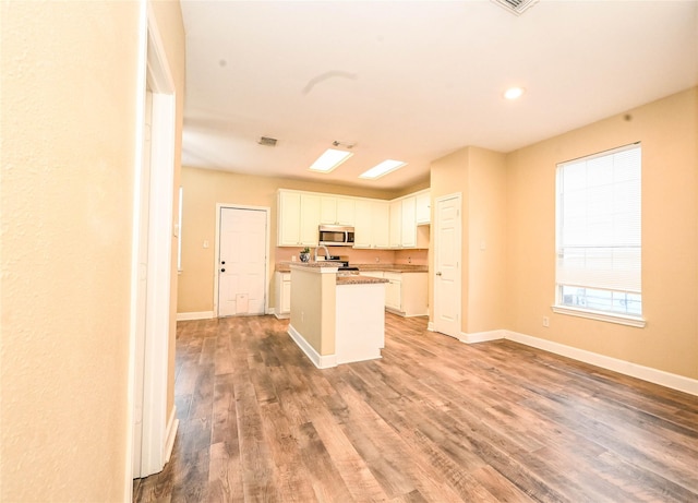 kitchen with white cabinetry, an island with sink, stainless steel appliances, and hardwood / wood-style flooring