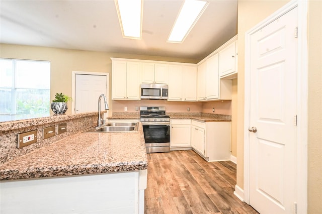 kitchen with sink, light hardwood / wood-style flooring, appliances with stainless steel finishes, light stone counters, and white cabinetry