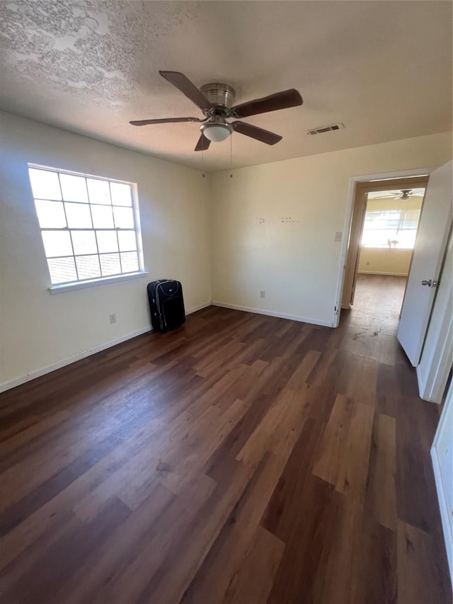 empty room with ceiling fan, dark hardwood / wood-style flooring, a healthy amount of sunlight, and a textured ceiling