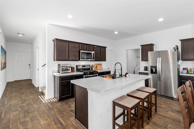 kitchen with sink, dark wood-type flooring, stainless steel appliances, a kitchen breakfast bar, and a kitchen island with sink