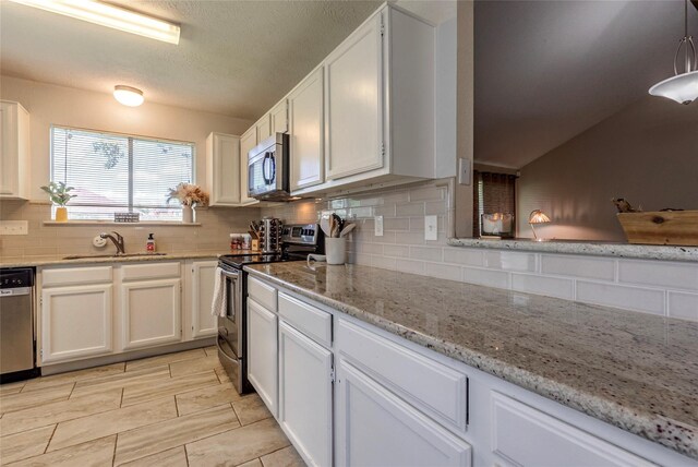 kitchen featuring light stone countertops, appliances with stainless steel finishes, tasteful backsplash, sink, and white cabinets