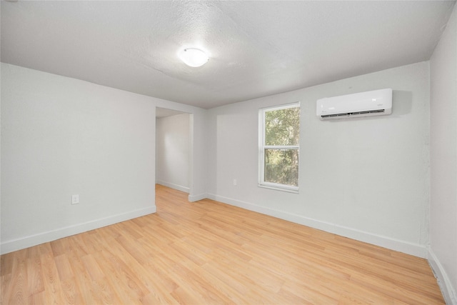 spare room with a wall unit AC, light hardwood / wood-style floors, and a textured ceiling