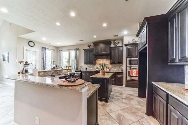 kitchen with dark brown cabinets, a center island with sink, and light stone counters