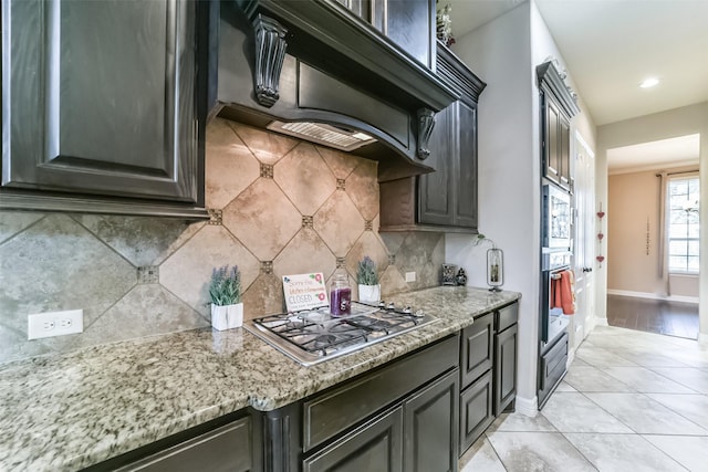 kitchen featuring backsplash, light stone counters, premium range hood, and appliances with stainless steel finishes