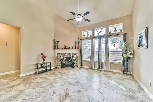 unfurnished living room with a stone fireplace, ceiling fan, light tile patterned floors, and a high ceiling