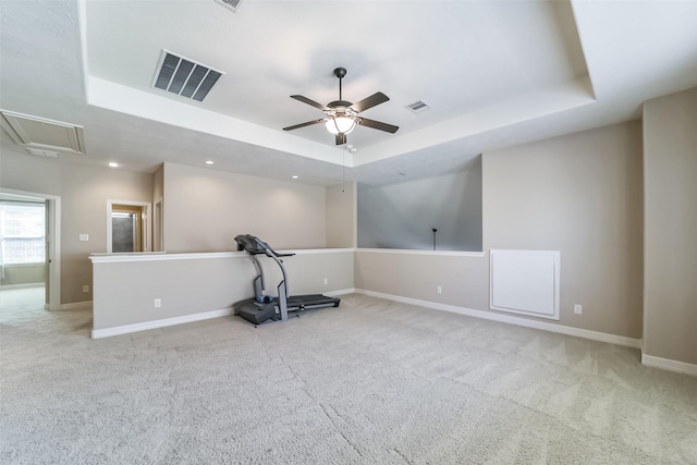 workout area with ceiling fan, a raised ceiling, and light carpet