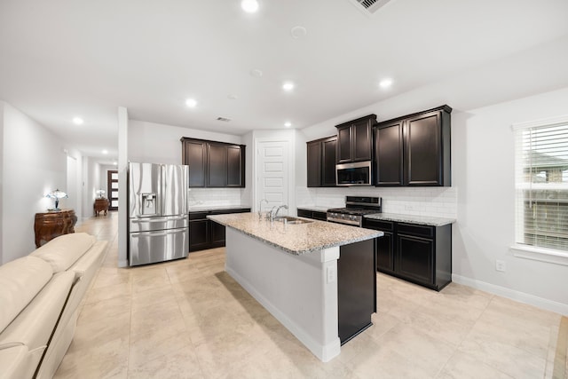 kitchen with appliances with stainless steel finishes, backsplash, dark brown cabinets, a kitchen island with sink, and sink