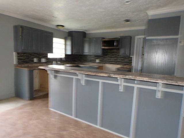 kitchen with gray cabinetry, a kitchen bar, kitchen peninsula, and ornamental molding