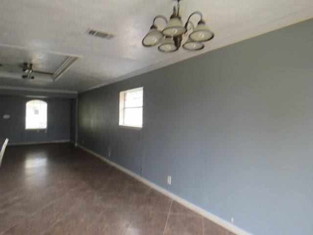 spare room with a notable chandelier, a healthy amount of sunlight, dark tile patterned floors, and a tray ceiling