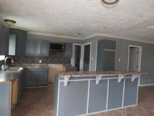 kitchen featuring backsplash, gray cabinets, ornamental molding, and sink