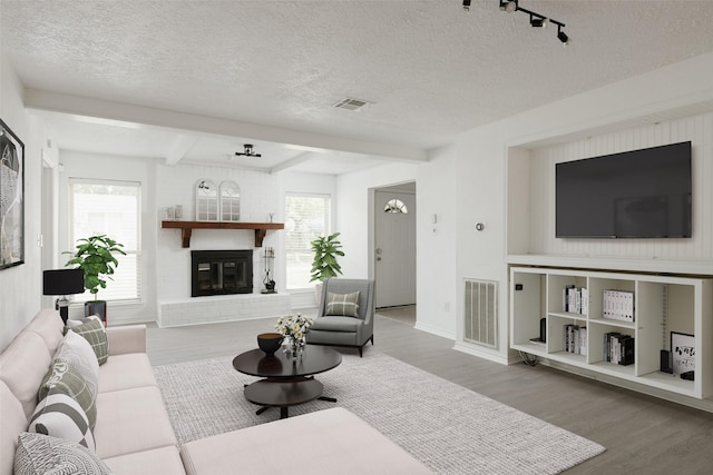 living room with beam ceiling, a textured ceiling, a brick fireplace, and wood-type flooring