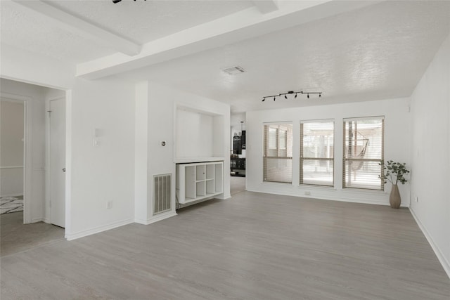 unfurnished living room featuring hardwood / wood-style flooring, beam ceiling, a textured ceiling, and track lighting