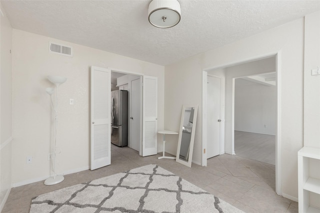 unfurnished bedroom featuring stainless steel fridge, light tile patterned flooring, and a textured ceiling