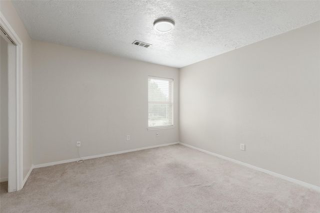 spare room featuring light colored carpet and a textured ceiling