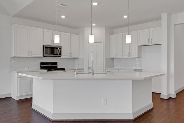 kitchen with sink, decorative light fixtures, stove, and a kitchen island with sink