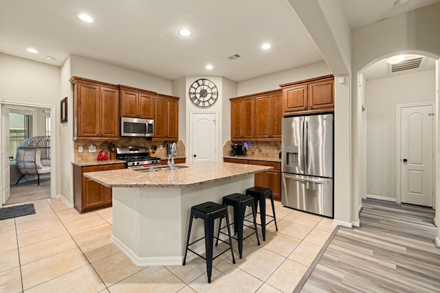 kitchen with decorative backsplash, light stone counters, an island with sink, and appliances with stainless steel finishes