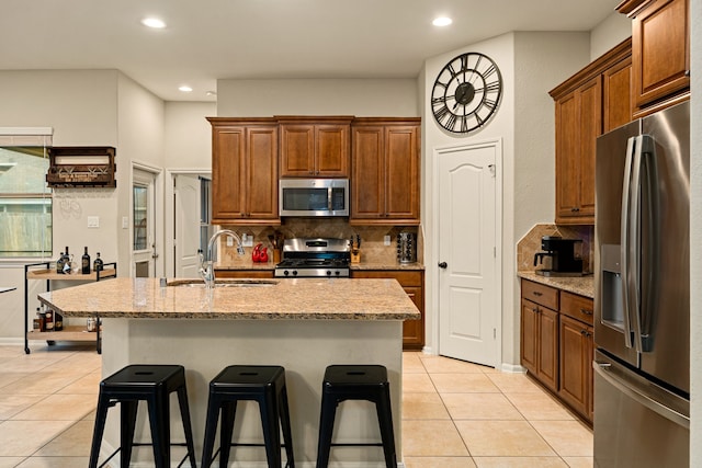 kitchen featuring a center island with sink, decorative backsplash, light tile patterned floors, and appliances with stainless steel finishes