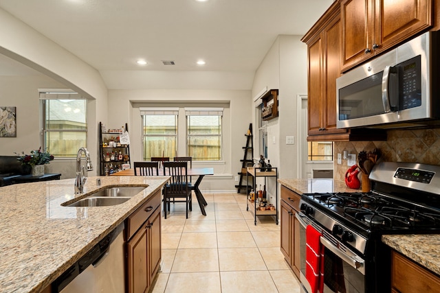 kitchen with sink, decorative backsplash, light tile patterned floors, light stone counters, and stainless steel appliances