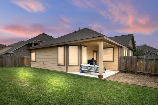 back house at dusk with a lawn and a patio area