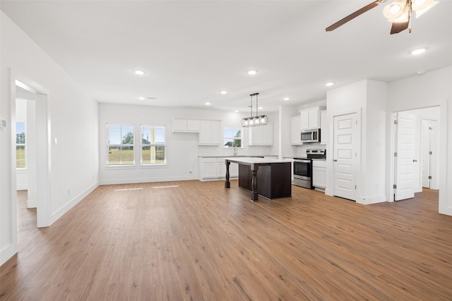 kitchen with a center island, decorative light fixtures, stainless steel appliances, a breakfast bar area, and white cabinets