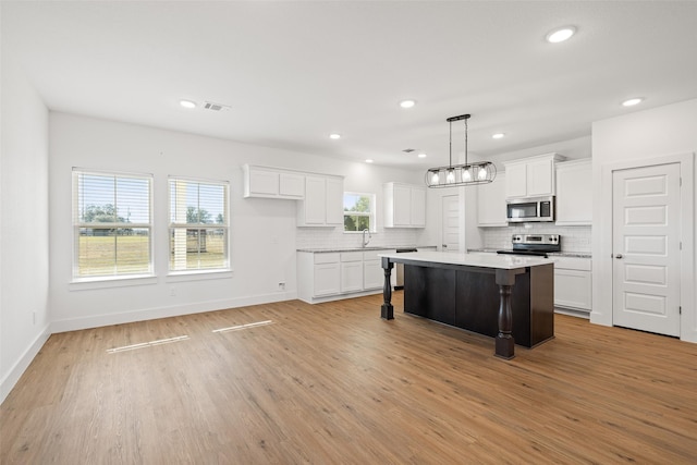 kitchen with pendant lighting, a kitchen island, a breakfast bar area, appliances with stainless steel finishes, and white cabinetry