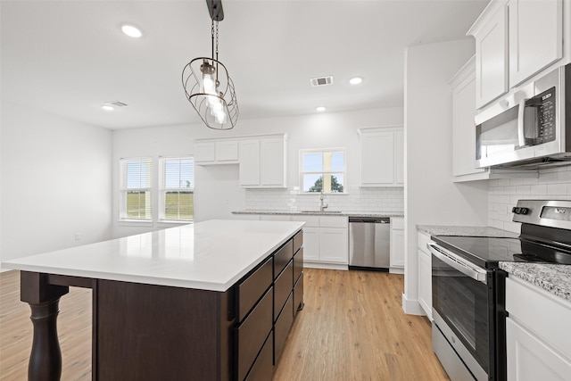 kitchen featuring a center island, decorative light fixtures, white cabinets, appliances with stainless steel finishes, and sink