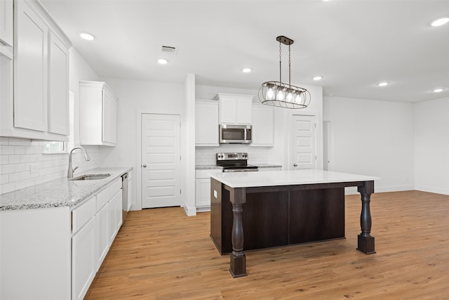 kitchen with sink, white cabinets, a center island, decorative light fixtures, and appliances with stainless steel finishes