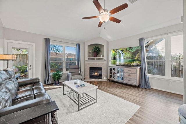 living room with hardwood / wood-style flooring, ceiling fan, lofted ceiling, and a tiled fireplace