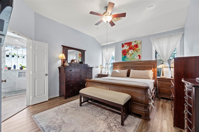 bedroom featuring light wood-type flooring, ensuite bathroom, ceiling fan, and lofted ceiling