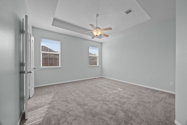 carpeted spare room featuring a raised ceiling and ceiling fan