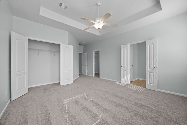 unfurnished bedroom featuring a raised ceiling, ceiling fan, and light carpet