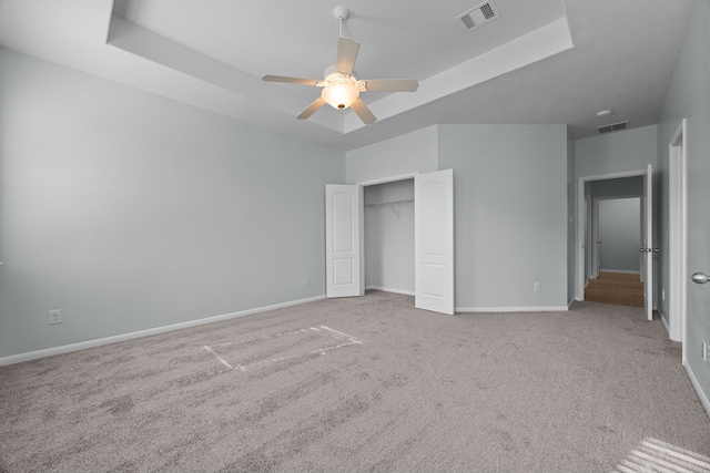 unfurnished bedroom with light carpet, a closet, a tray ceiling, and ceiling fan