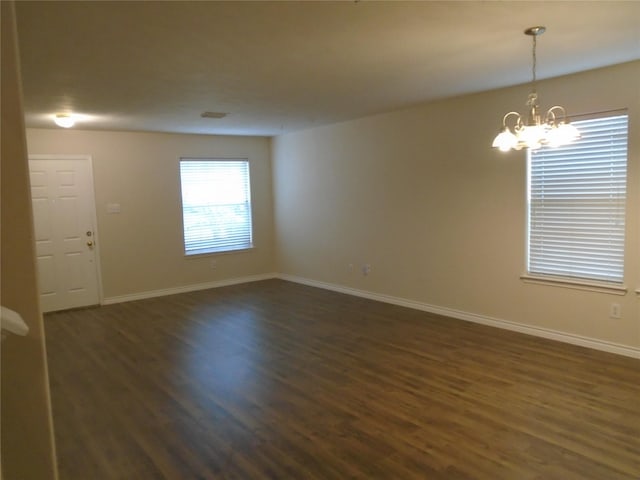 empty room featuring a notable chandelier and dark wood-type flooring