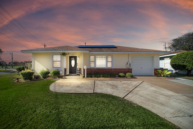 ranch-style home with a yard, a garage, and solar panels