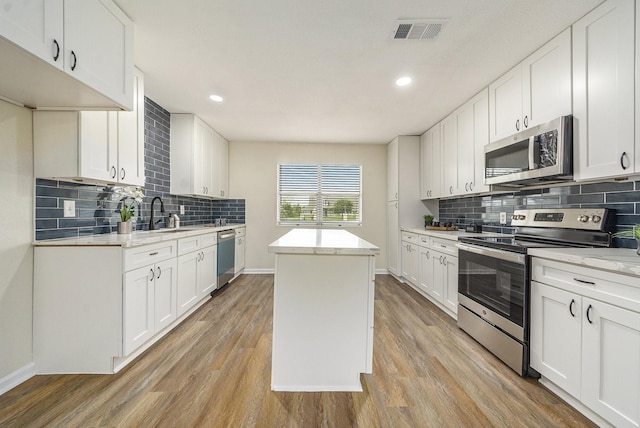 kitchen featuring white cabinets, light hardwood / wood-style flooring, appliances with stainless steel finishes, tasteful backsplash, and a kitchen island