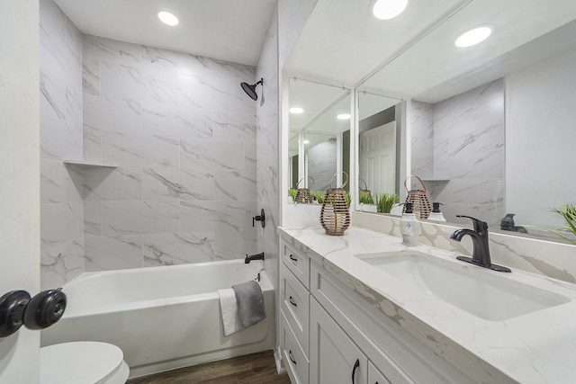 full bathroom featuring vanity, hardwood / wood-style floors, tiled shower / bath combo, and toilet