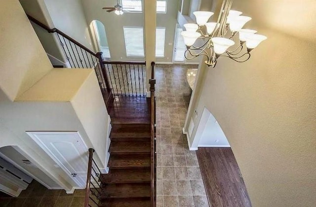 stairs with ceiling fan with notable chandelier and a towering ceiling